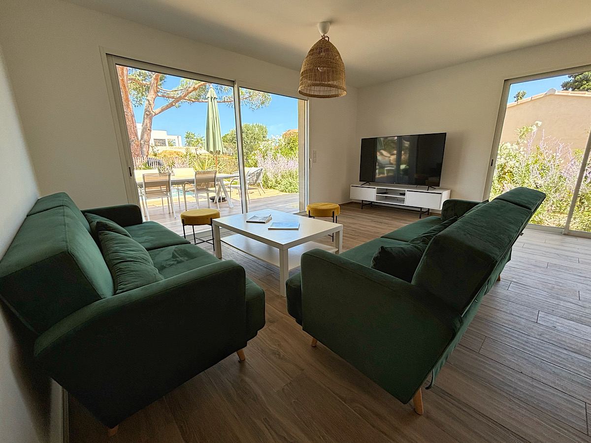 Salon moderne équipé d'un canapé de chez Cuir center 6 assises, d'un télévision murale connectée. Le salon offre une vue complète sur la terrasse piscine et la baie de Calvi