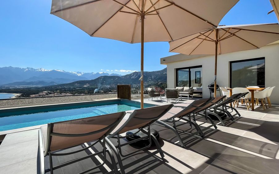 Grande terrasse et sa piscine avec une vue à couper le souffle sur la baie de Calvi. La terrasse offre des bains de soleil, une table à manger, un salon de jardin. Une vraie continuité avec la pièce de vie de la villa.