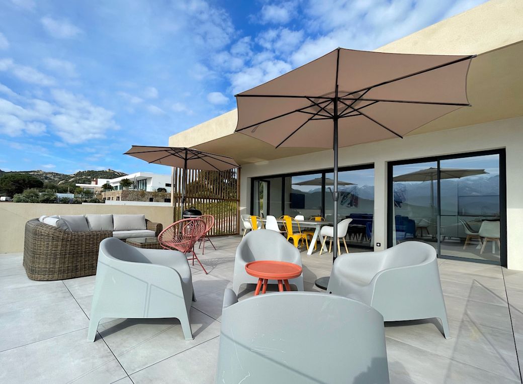 Terrasse équipée avec bains de soleil, table à manger extérieure, salon de jardin et une vue panoramique que la baie de Calvi